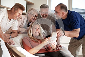 Happy mature woman showing photos to her friends .