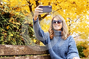 Happy mature woman sitting on the bench outdoor and making a self portrait