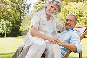 Happy mature woman sitting on her husband on deck chair