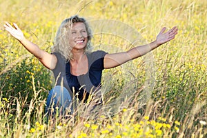 Happy mature woman spreading her arms in a meadow