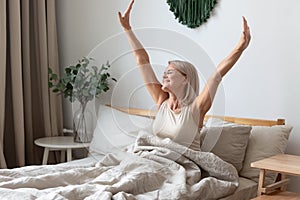 Happy mature woman stretching in bed waking up happy concept photo