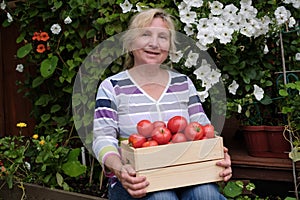 Happy mature woman with tomato harvest sitting in garden