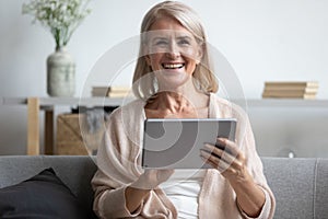 Happy mature woman using computer tablet, laughing at funny joke