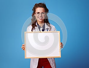 Happy medical doctor woman showing blank board on blue