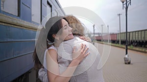 Happy meeting, joyful young woman hugs male and laughs near train wagon on railway station after separation