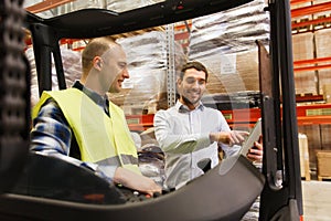 Happy men with tablet pc and forklift at warehouse