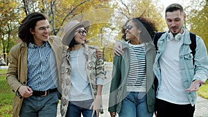 Happy men and women walking in park talking gesturing enjoying communication