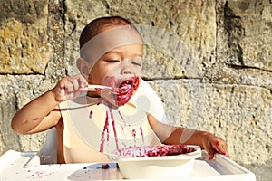 Happy messy baby boy eating blueberry cake with spoon