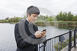 Happy mid adult businessman text messaging through mobile phone at bridge railing