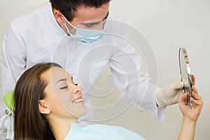 Happy mid adult female patient with doctor looking at mirror in clinic