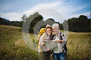 Happy mid adult woman with active senior mother hiking and looking at map outdoors in nature.