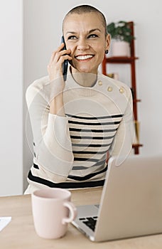 Happy mid adult woman talking on mobile phone sitting at office workplace