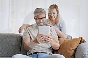 Happy mid aged couple relaxing on the sofa at home and using touchpad