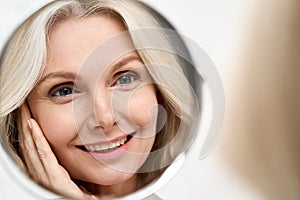 Happy mid aged woman looking at mirror. Antiaging beauty care concept.