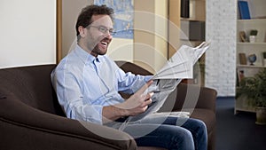 Happy mid-forties male reading newspaper, relaxed person sitting on sofa, press