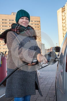 Happy middle age adult woman holding fuel pump by car at self-service gas station