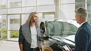 Happy middle age car salesperson came to an agreement with young long haired beard man in a showroom with new crossover