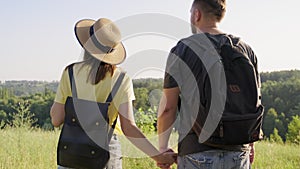 Happy middle age couple holding hands, man and woman with backpacks, back view