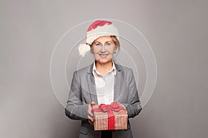 Happy middle age senior woman Santa holding Christmas present box and smiling over grey background