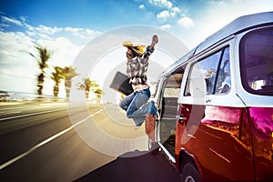 Happy middle age woman jumping outside a red vintage van while traveling fast on the road for the joy to start the vacation or