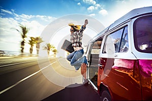 Happy middle age woman jumping outside a red vintage van while traveling fast on the road for the joy to start the vacation or