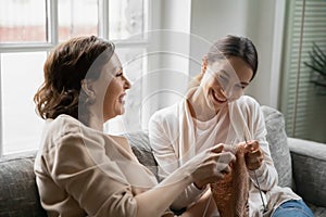 Happy middle aged 60s woman teaching grown daughter knitting.