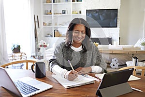 Happy middle aged African American  woman sitting at table in her dining room making notes, selective focus