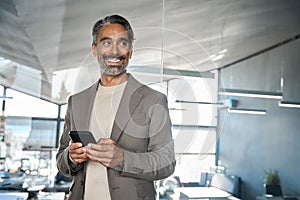 Happy middle aged business man using mobile cell phone in office looking away.