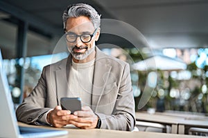 Happy middle aged business man using mobile phone sitting outside office.