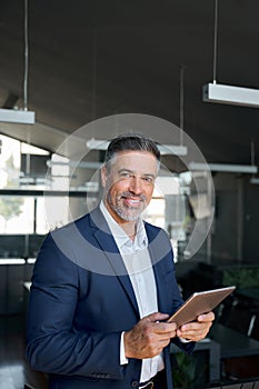 Happy middle aged business man wearing suit in office using digital tablet.