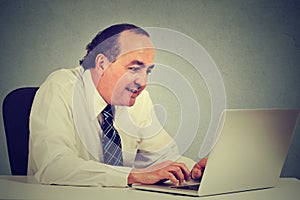 Happy middle aged businessman working with laptop in office