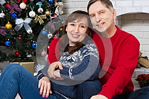 Happy middle-aged couple family hugging by the fireplace near the Christmas tree
