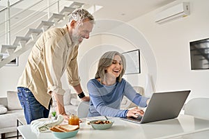 Happy middle aged couple having fun using laptop computer at home.