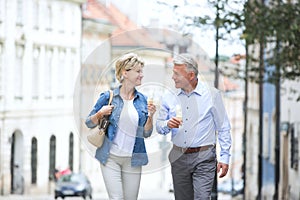 Happy middle-aged couple looking at each other while holding ice cream cones in city