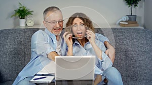 A happy middle-aged couple, looking at a laptop, feels like an online winner.