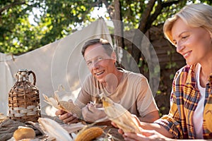 Happy middle-aged couple sitting at table, shucking corn