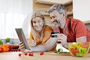 Happy middle aged couple using digital tablet and credit card