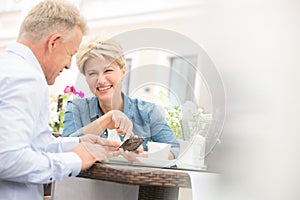 Happy middle-aged couple using mobile phone at sidewalk cafe