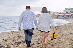 Happy middle aged couple walking together on the beach, back view