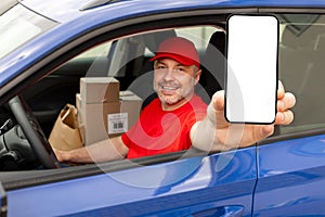 Happy middle aged courier man showing cellphone with empty screen, advertising delivery service, sitting in van and