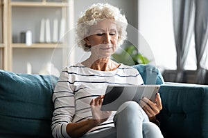Happy middle aged elderly retired woman using digital computer tablet.