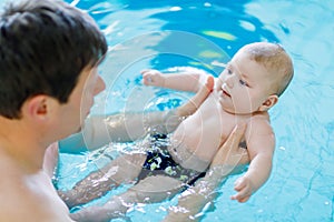 Happy middle-aged father swimming with cute adorable baby in swimming pool.