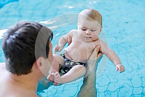 Happy middle-aged father swimming with cute adorable baby in swimming pool.