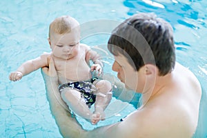 Happy middle-aged father swimming with cute adorable baby in swimming pool.