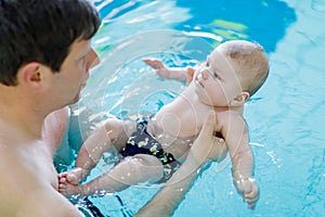 Happy middle-aged father swimming with cute adorable baby in swimming pool.