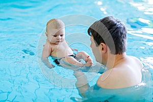 Happy middle-aged father swimming with cute adorable baby in swimming pool.