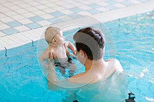 Happy middle-aged father swimming with cute adorable baby in swimming pool.