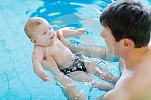 Happy middle-aged father swimming with cute adorable baby in swimming pool.