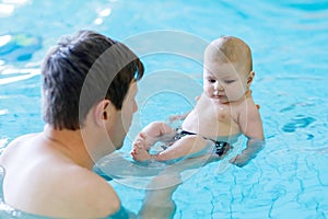 Happy middle-aged father swimming with cute adorable baby in swimming pool.