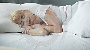 Happy middle-aged female sleeping in bed on orthopedic mattress, health